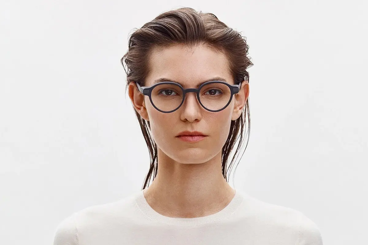 A frontal portrait of a woman wearing dark, round glasses, against a pure white background.