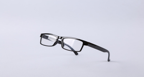 Minimalist black full-rim rectangular prescription glasses, suspended against a gray background.