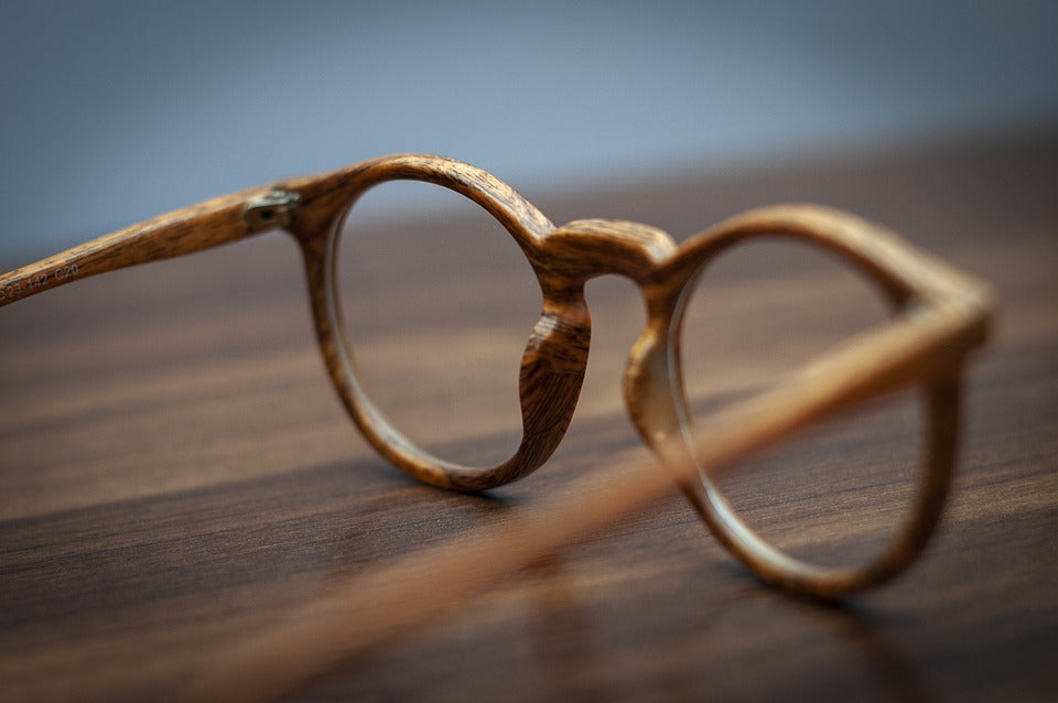 A close-up detail shot of round eyeglass frames with a wood-grain texture, showcasing exquisite natural wood patterns.