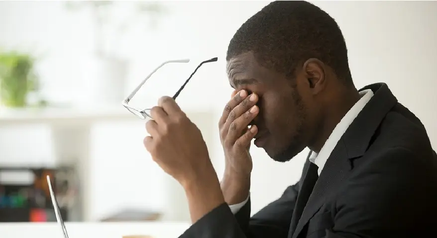 A man in a suit took off his glasses, closed his eyes, and rubbed them with his hands, displaying clear signs of eye strain.