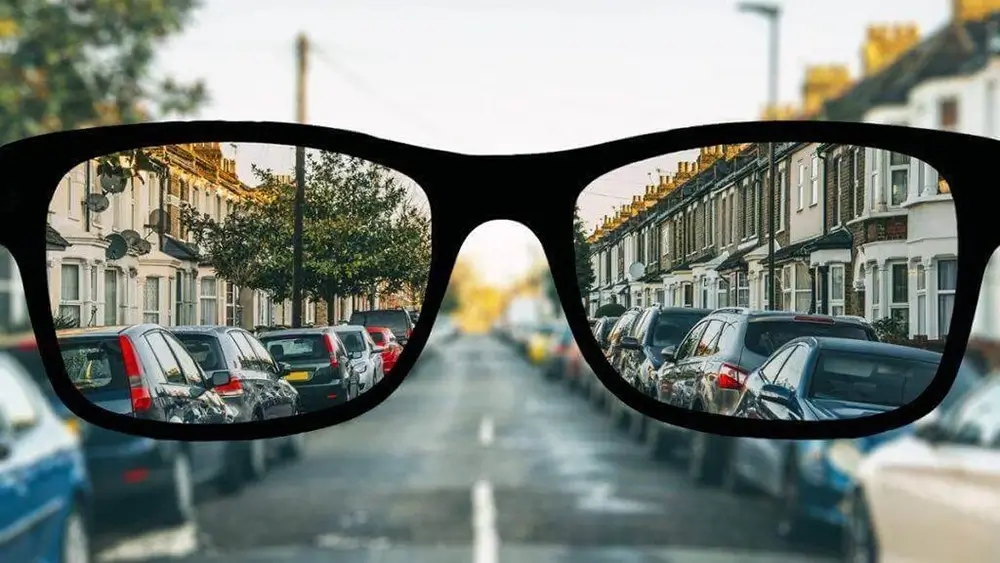 A pair of black-rimmed glasses focused sharply on rows of cars parked along a residential street.