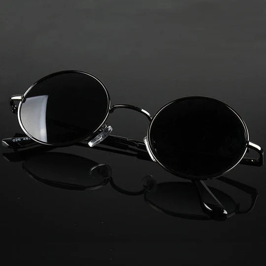 Round sunglasses with thin black metal frames, placed on a reflective black background.