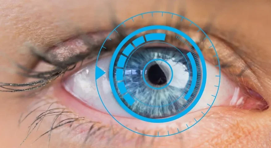 A close-up of a human eye, featuring a superimposed blue digital-tech scanning ring and data charts on the iris, symbolizing ophthalmic pupillary measurement.