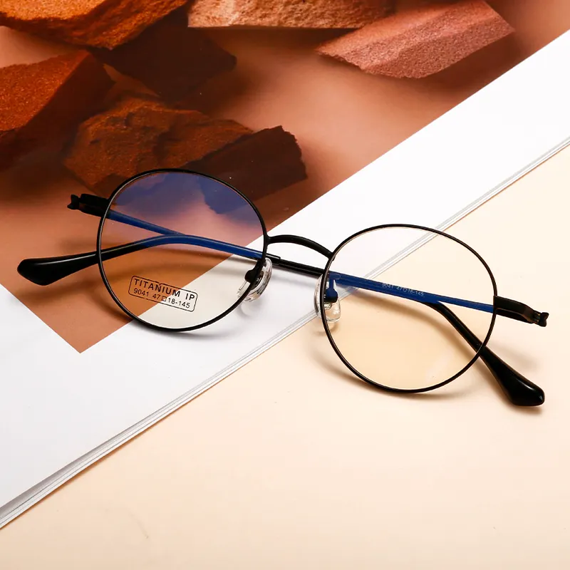 A pair of minimalist black glasses with thin metal round frames, resting on a flat surface, featuring a "TITANIUM IP" label affixed to the lenses.