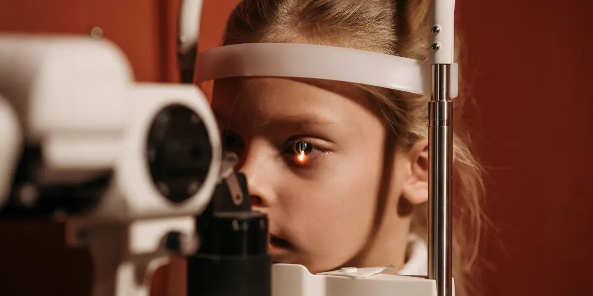 A close-up of a young girl undergoing an eye examination at an eye clinic, with light shining on her eyes.