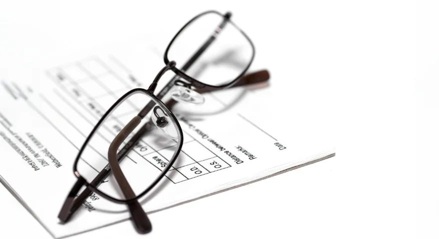 A pair of rectangular glasses rests on an eyeglass prescription slip.
