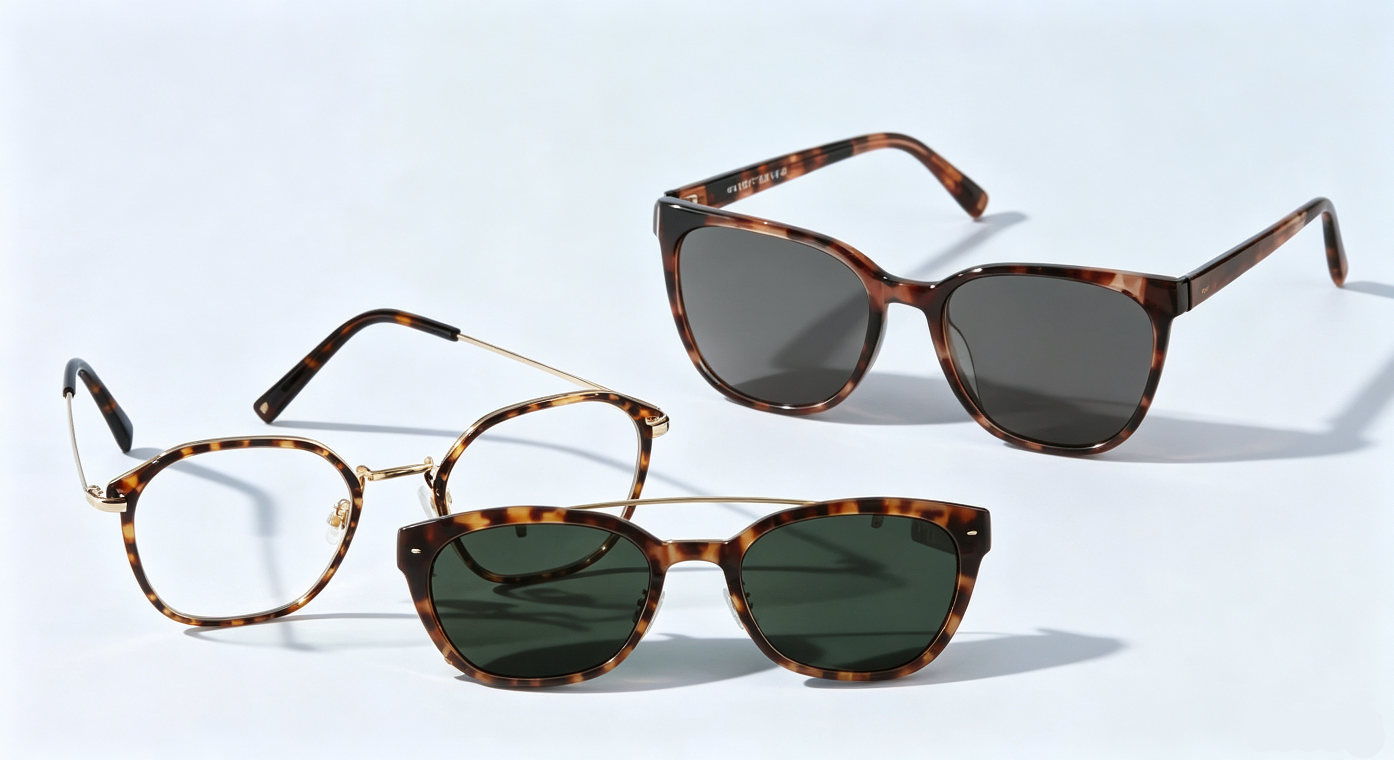 Tortoiseshell optical glasses with a clip-on sun lens and a pair of dark-lens sunglasses, displayed on a light-colored background.