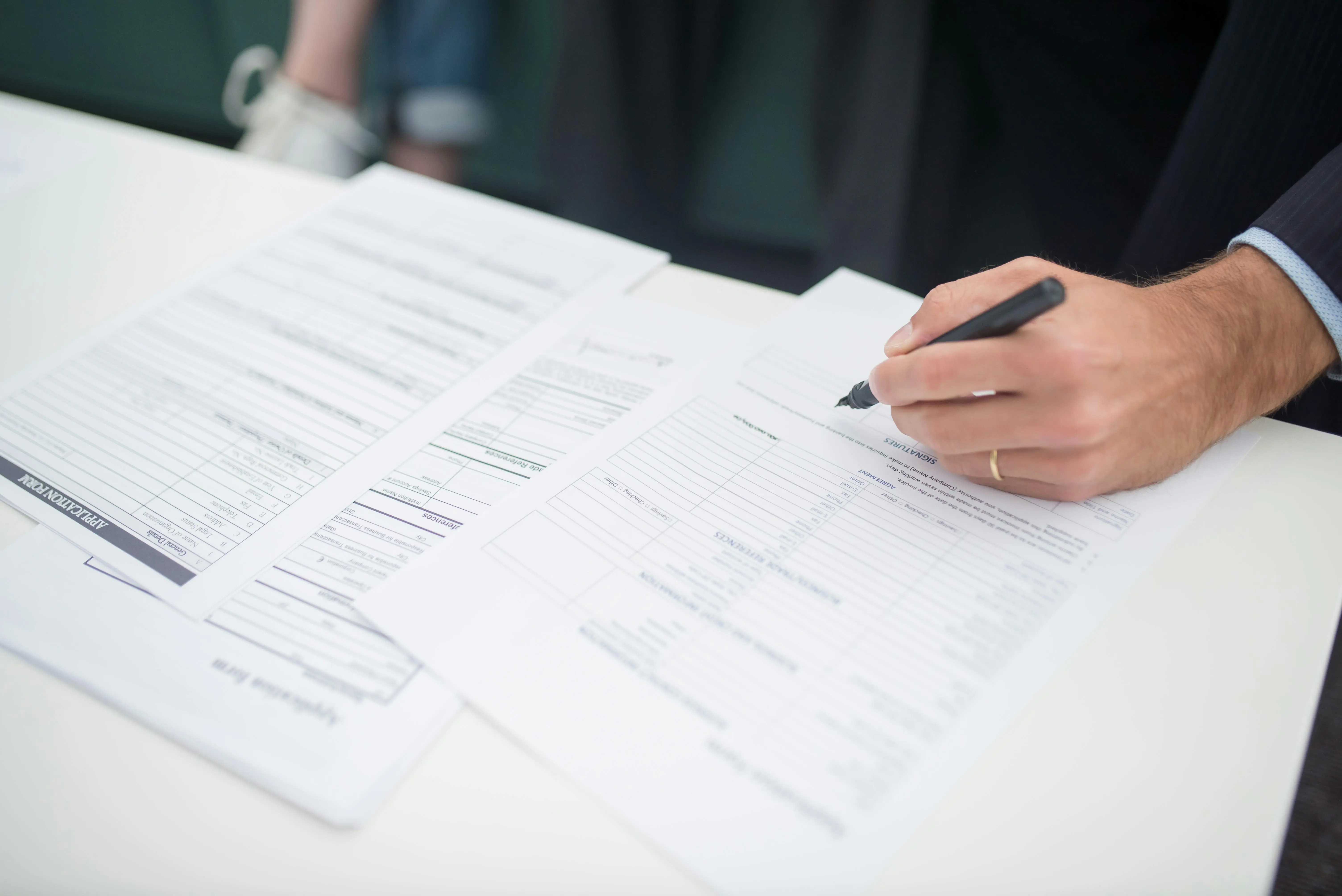 A person wearing a wedding ring is signing a vision insurance policy on an office desk with a black pen.