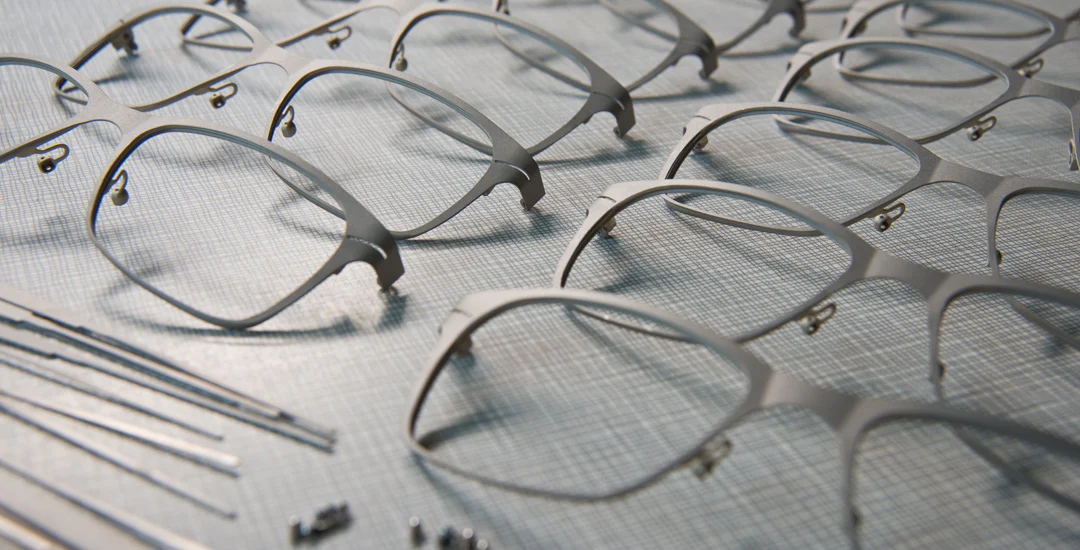 Finished minimalist metal eyeglass frames, neatly arranged against a brushed gray background.