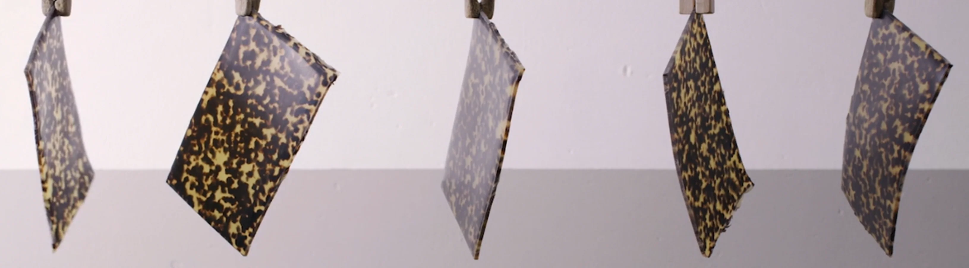 Four tortoiseshell-patterned sheets of varying textures (raw materials for eyewear) hang vertically against a light-colored background.