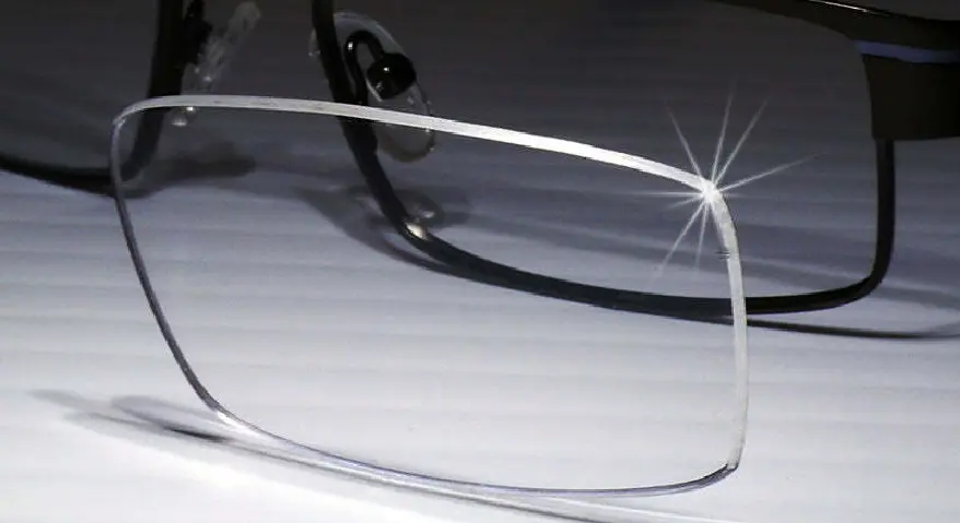 A close-up shot of an eyeglass lens featuring an anti-reflective coating, with the edges of the lens shimmering with a crystalline sparkle under the light.