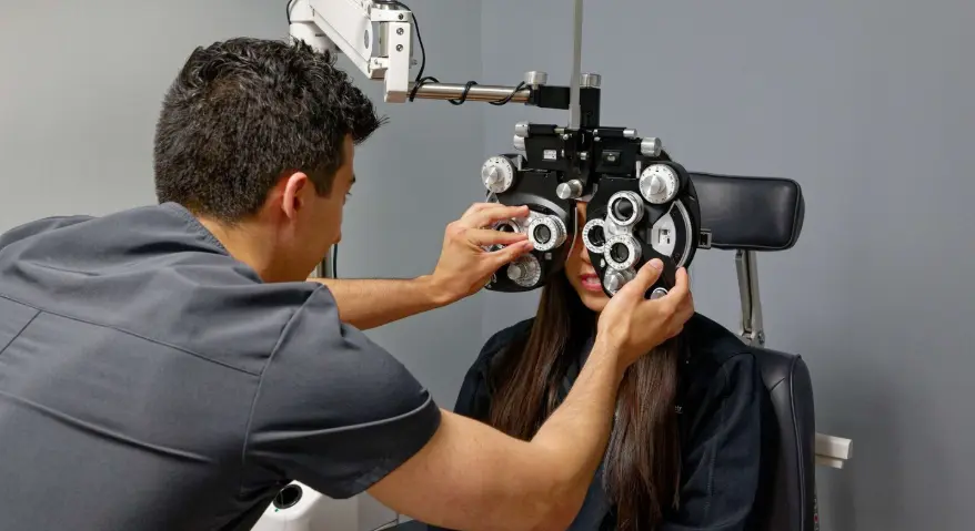 Optometry Scene: A professional optometrist is operating a phoropter to conduct a vision examination for a young woman seated behind the instrument.