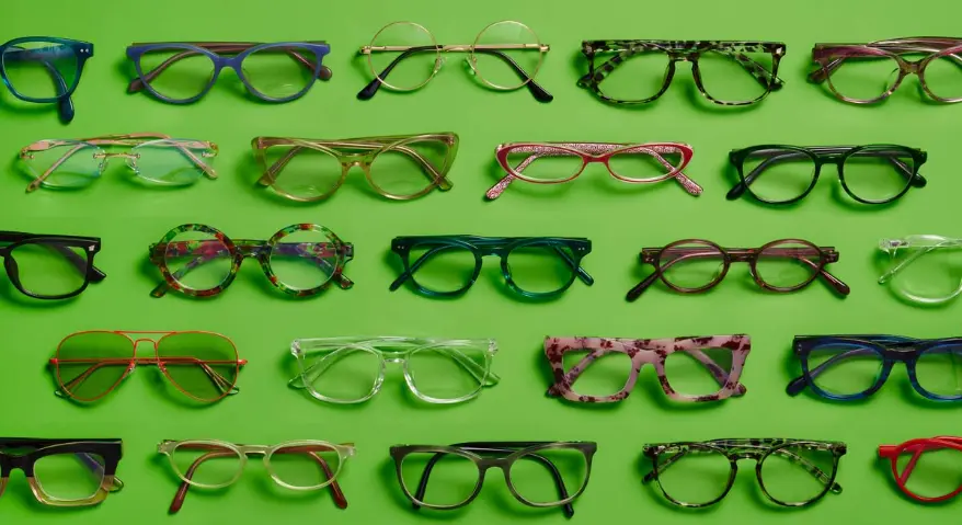 A top-down view of various eyeglass frames—differing in style, color, and material—neatly arranged against a green background, including transparent, leopard-print, bright-colored, and thin metal frames.