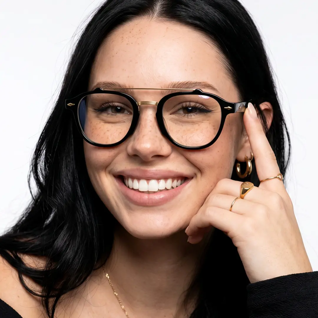 Front view of female wearing vintage black aviator eyeglasses, touching frame, smiling, AA0142603