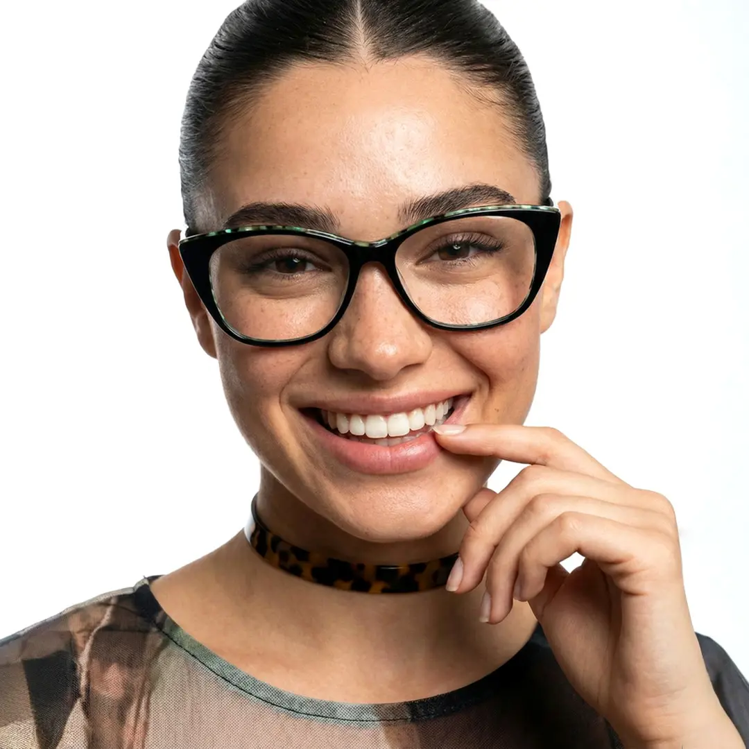 Front view of female wearing black cat eye eyeglasses, finger on lips, smiling, CA0012208