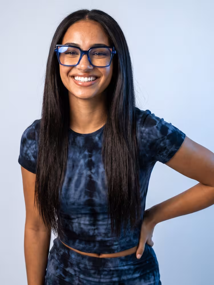 Female model wearing colorful blue cat eye acetate eyeglasses in a dark tie-dye crop top smiling with hand on hip against a light blue studio background. SPU: CA0342605