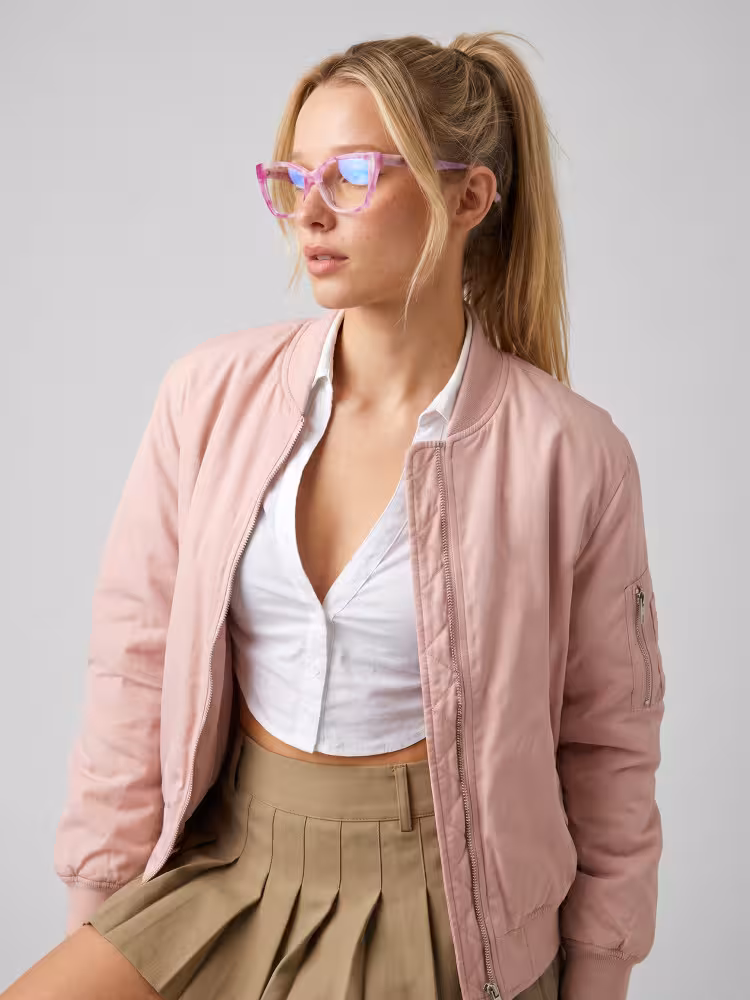 Female model wearing colorful pink cat eye acetate eyeglasses in a pink bomber jacket and khaki pleated skirt looking aside against a plain grey studio background. SPU: CA0432605