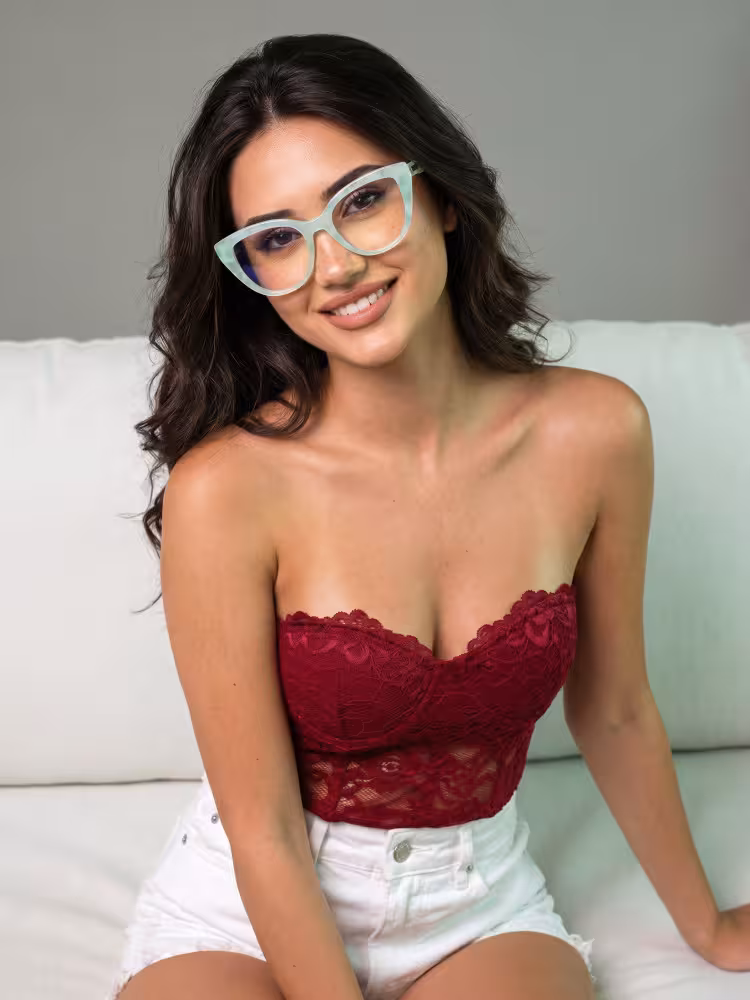 Female model wearing colorful green cat eye acetate eyeglasses in a burgundy lace corset top smiling on a white sofa against a grey studio background. SPU: CA0442605