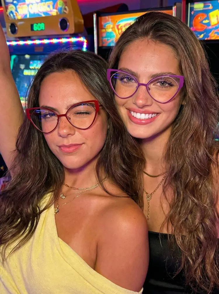 Two people models wearing elton john purple and red cat eye metal eyeglasses in a retro arcade with neon lights. SPU: CM0042311