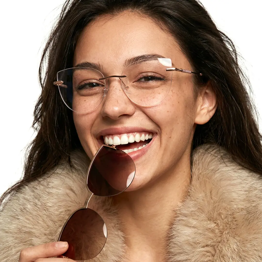 Close-up view of female wearing gold cat eye magnetic clip-on eyeglasses set with interchangeable toppers, holding topper, big smile, CM0272601