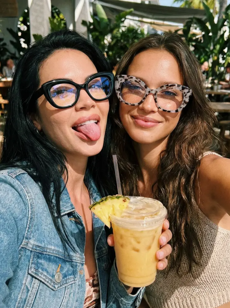 Two people model wearing colorful black and grey tortoise cat eye pc eyeglasses in a denim jacket and a knit top holding a tropical drink at an outdoor resort cafe. SPU: CP0302403