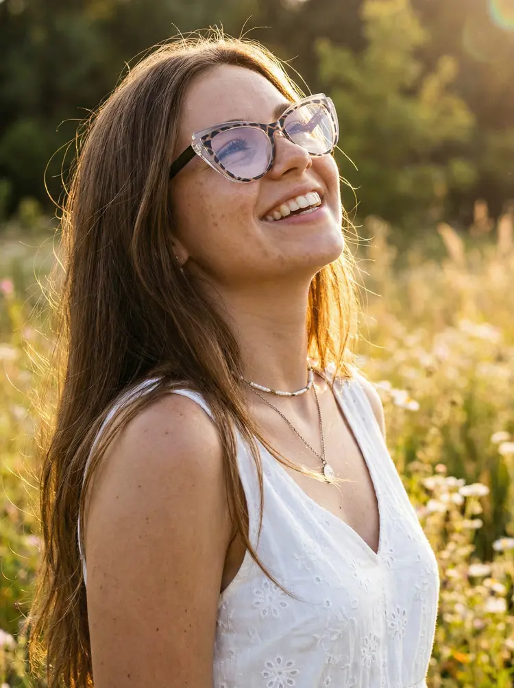 Female model wearing everyday tortoise cat eye tr90 eyeglasses in a white embroidered V-neck dress laughing in a sunlit flower field at sunset. SPU: CR0052403