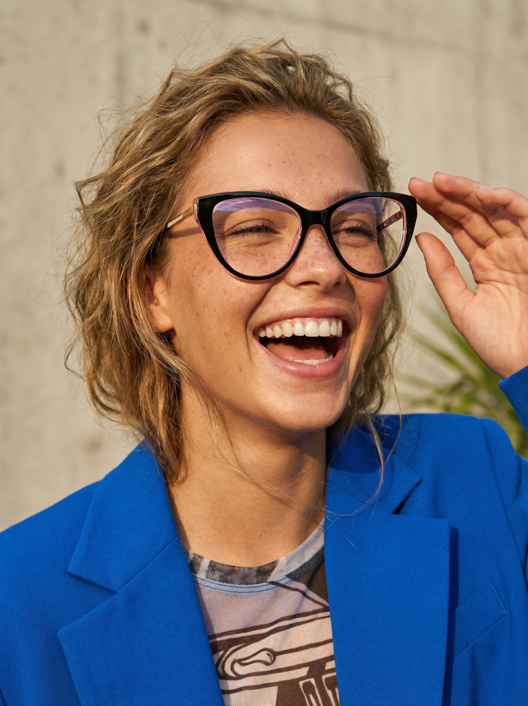 Female model wearing everyday eyewear black cat eye tr90 eyeglasses against an urban concrete wall. SPU: CR0112408