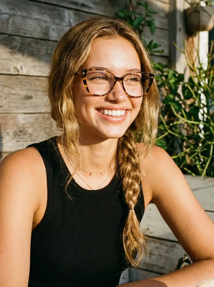 Female model wearing everyday tortoise cat eye tr90 eyeglasses outdoors against a wooden wall. SPU: CR0252411