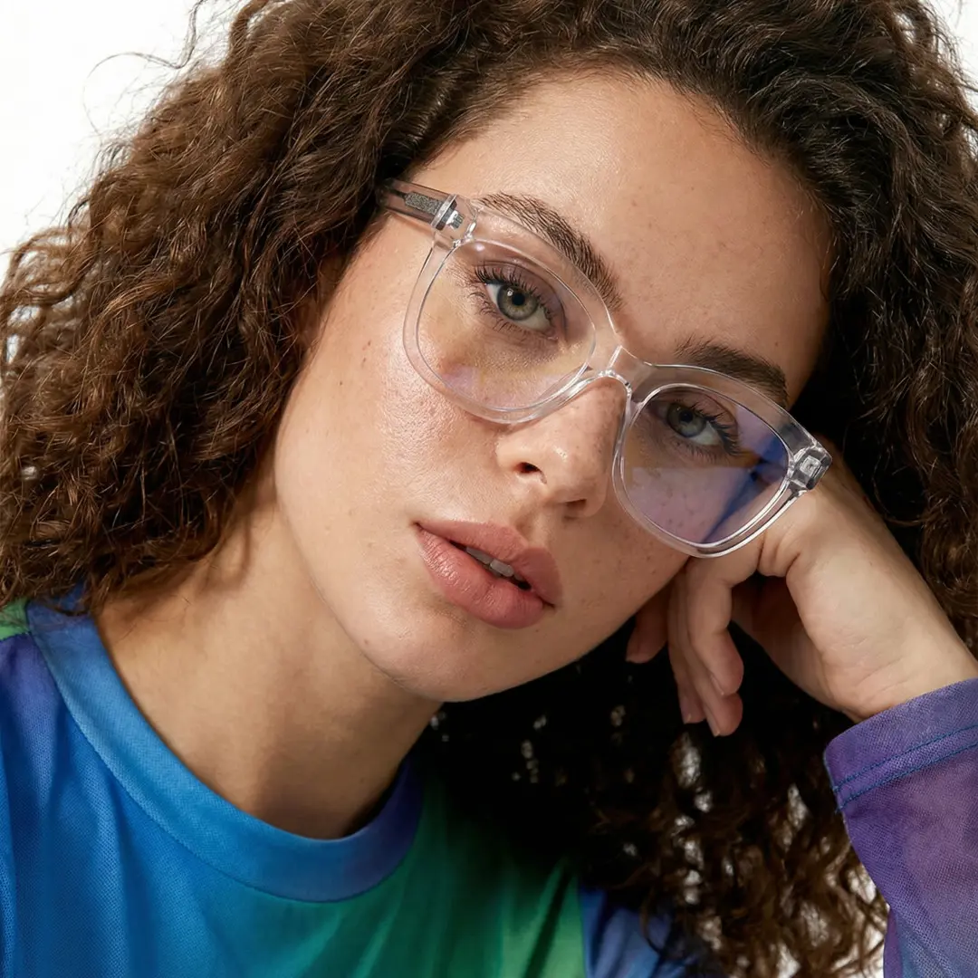 Close-up view of female wearing clear cat eye eyeglasses, hand near face, neutral expression, CR0532505