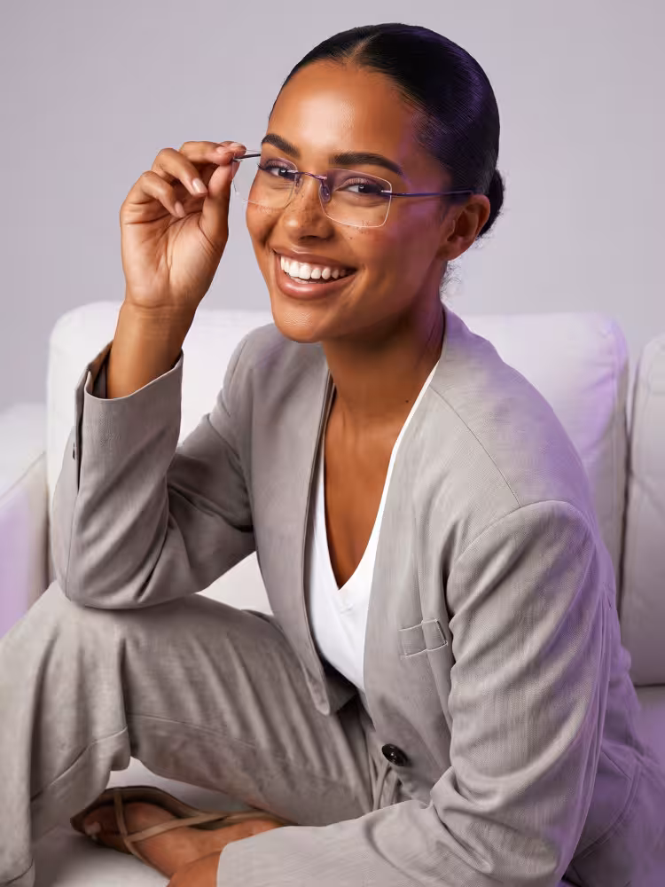 Female model wearing office siren pink rectangle metal eyeglasses in an indoor lounge space beside a plush white sofa. SPU: EM0172605