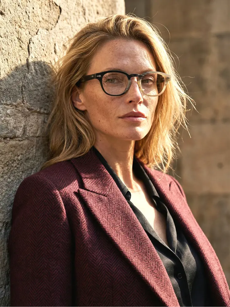 Female model wearing luxury two-tone rectangle natural ox horn handcrafted eyeglasses leaning against an old stone wall in warm outdoor sunlight. SPU: EO0252511
