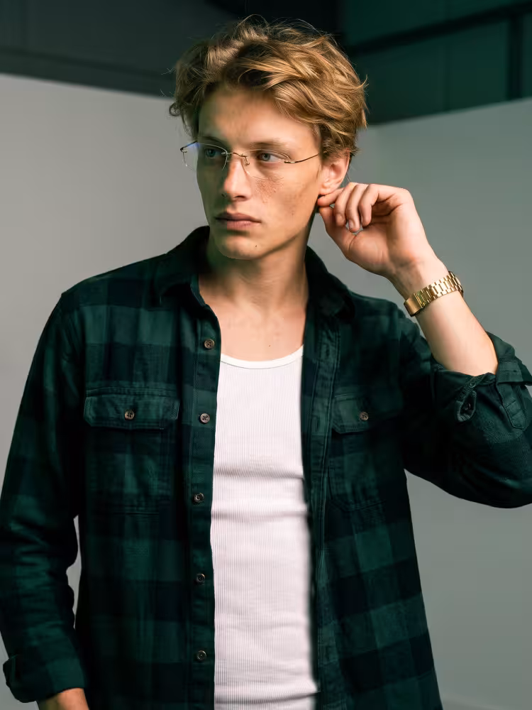 Male model wearing casual gold rectangle titanium eyeglasses in an indoor portrait studio with dark green overhead panels and light gray wall background. SPU: ET0242605
