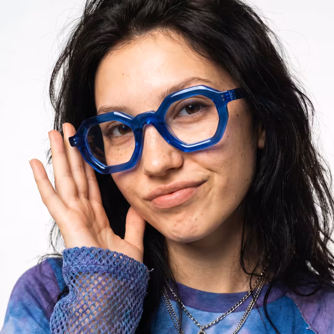 Front view of female wearing blue geometric eyeglasses, touching frame, soft smile, GA0052310