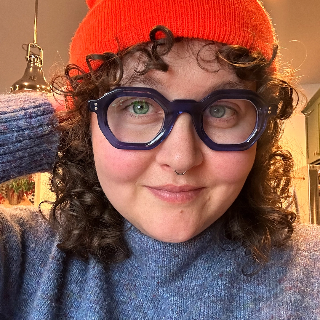 Front view of female wearing blue geometric eyeglasses, hand in hair, smiling, GA0052310