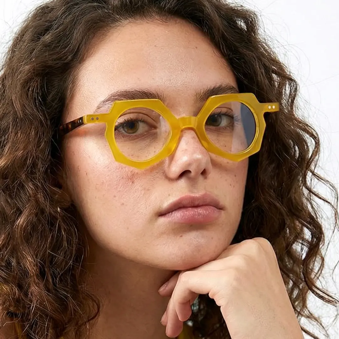 Three-quarter view of female wearing yellow geometric eyeglasses, resting chin on hand, neutral expression, GA0062309