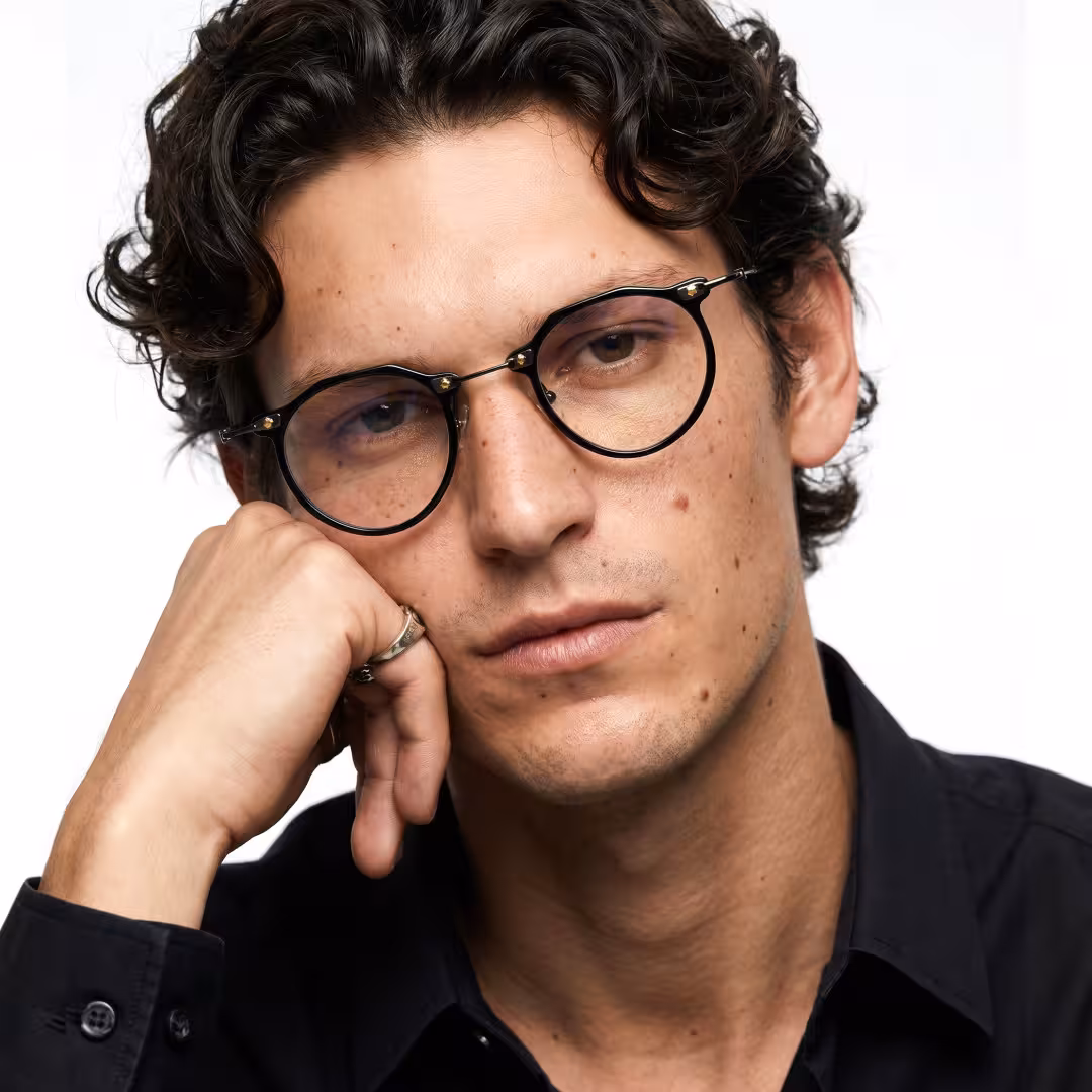 Front view of male wearing steampunk black geometric eyeglasses, hand near face, neutral expression, GA0072307