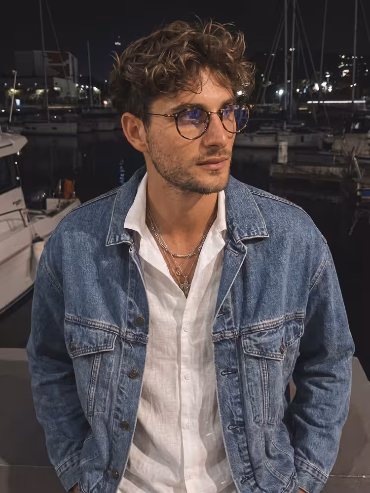 Male model wearing steampunk tortoise geometric acetate eyeglasses at a nighttime harbor with docked yachts . SPU: GA0072307