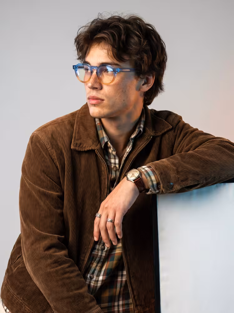 Male model wearing colorful blue gradient geometric acetate eyeglasses with brown corduroy jacket and plaid shirt against neutral gray studio background. SPU:GA0072310