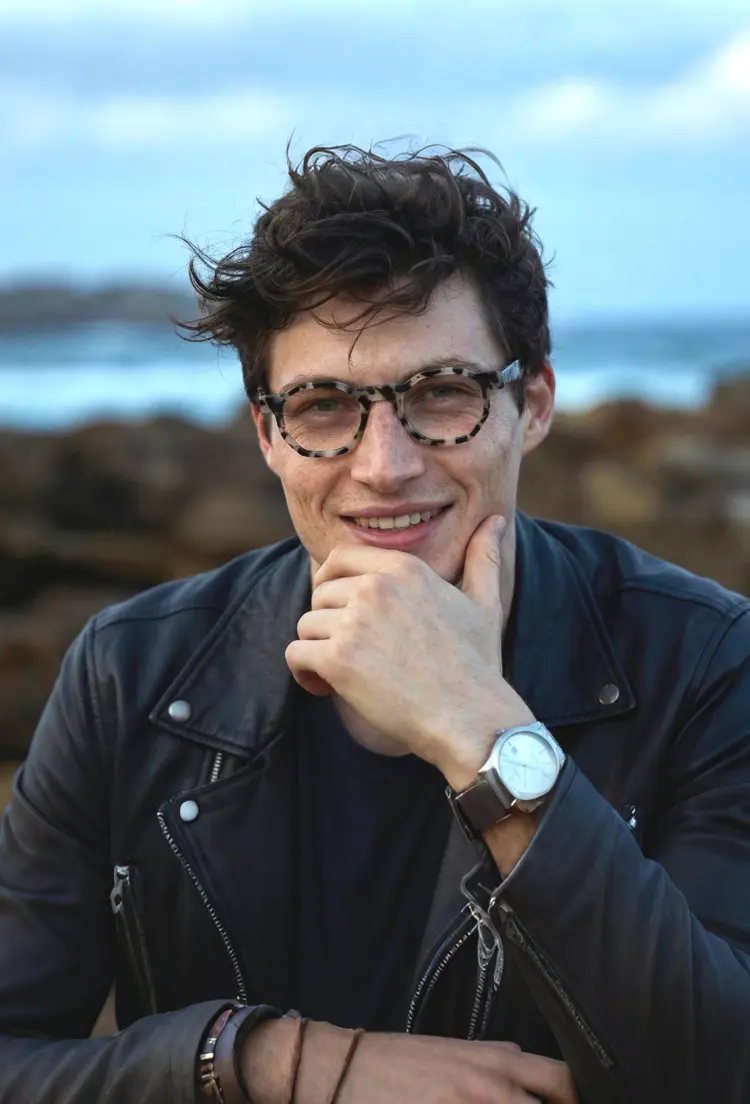 Male model wearing everyday tortoise geometric acetate eyeglasses in a black leather jacket with hand on chin on a rocky beach background. SPU: GA0172406