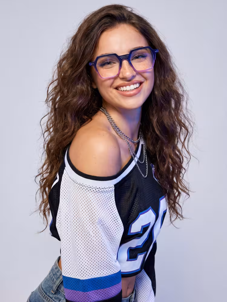Female model wearing colorful purple geometric eyeglasses in a professional photo studio with neutral gray background. SPU: GA0412503