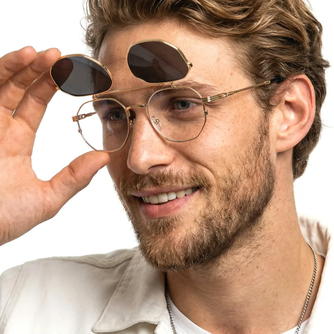Three-quarter view of male wearing gold geometric flip-up eyeglasses, touching frame, natural smile, GM0052601
