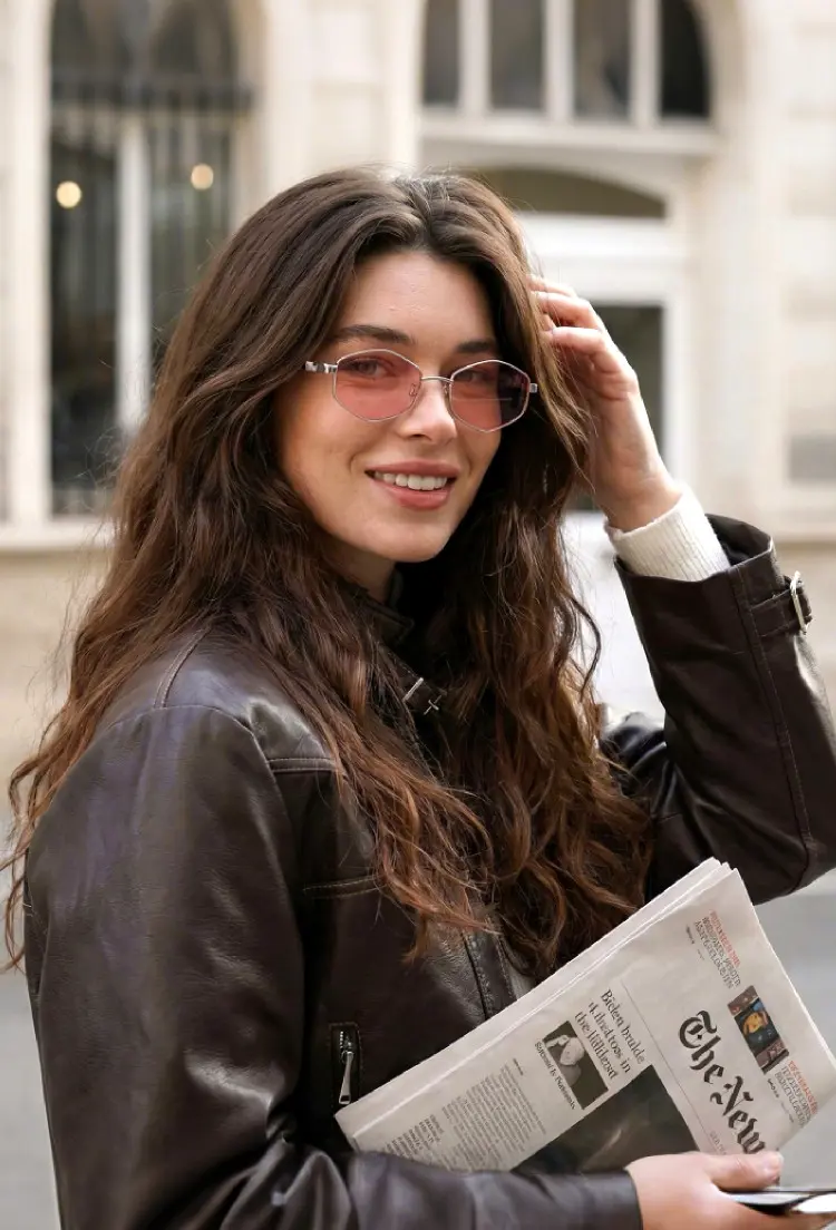 Female model wearing fashion clear geometric metal eyeglasses holding a newspaper on a European city street. SPU: GM0062601
