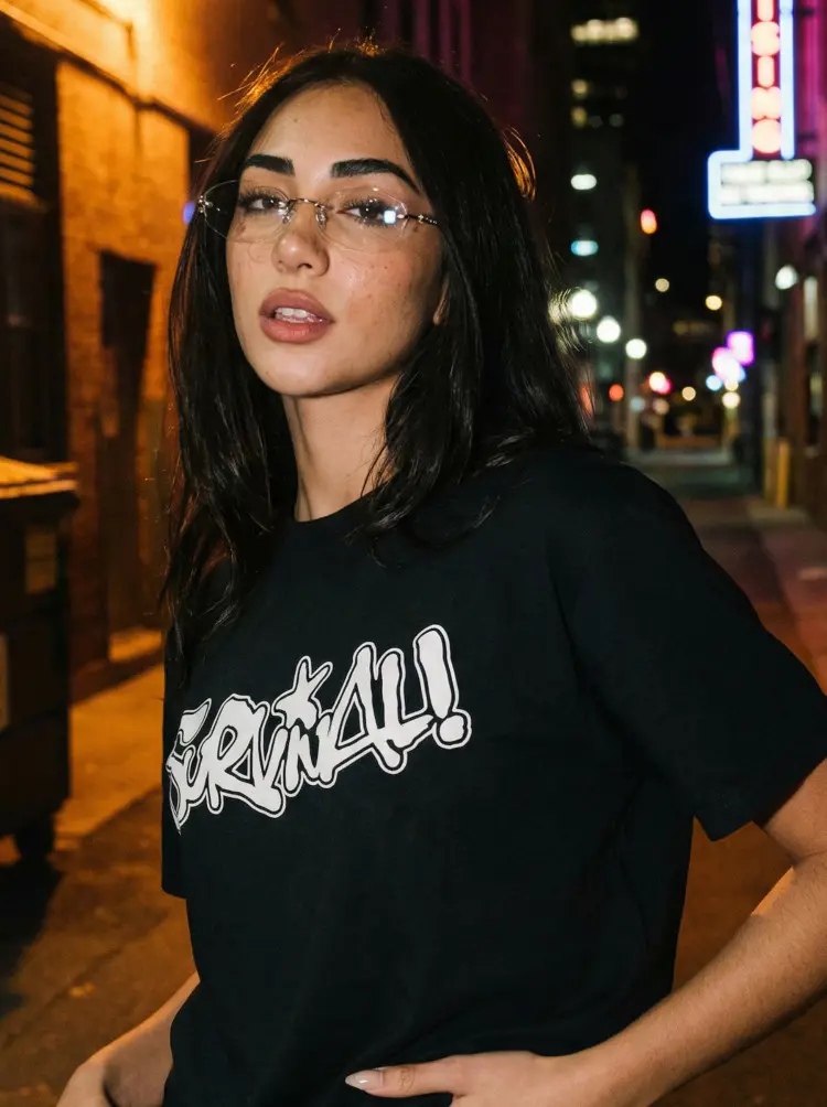 Female model wearing fashion silver geometric metal eyeglasses in a black graphic t-shirt standing on a city street at night with neon lights. SPU: GM0192601