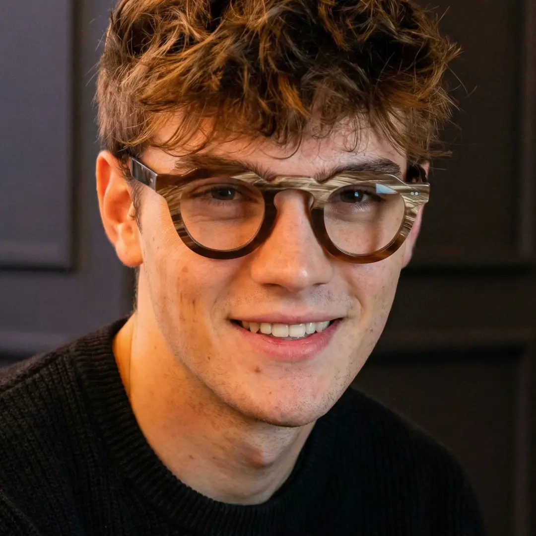 Looking away view of male wearing brown geometric natural ox horn handcrafted eyeglasses, smiling, GO0272511