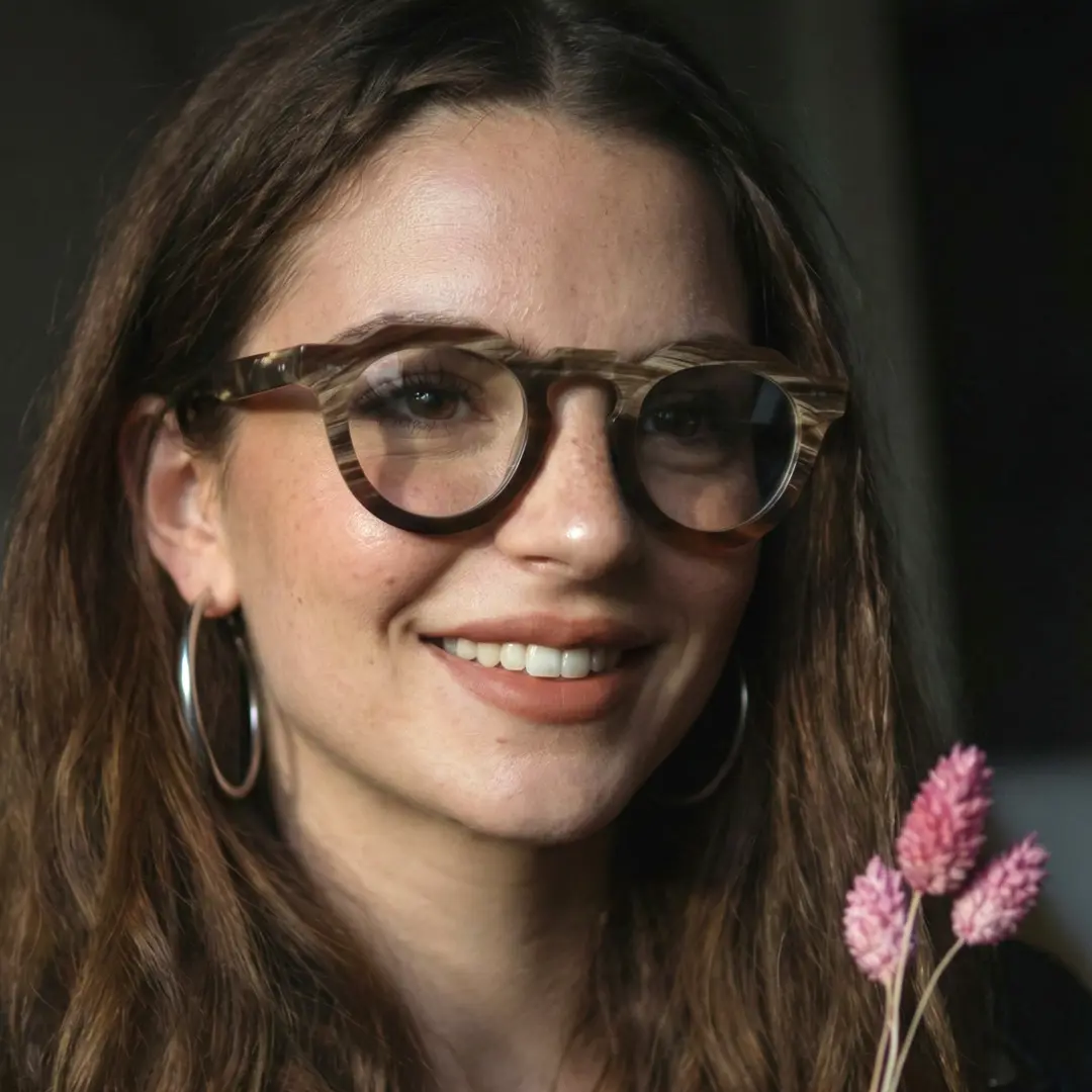 Face close-up view of female wearing brown geometric natural ox horn handcrafted eyeglasses, friendly smile, GO0272511