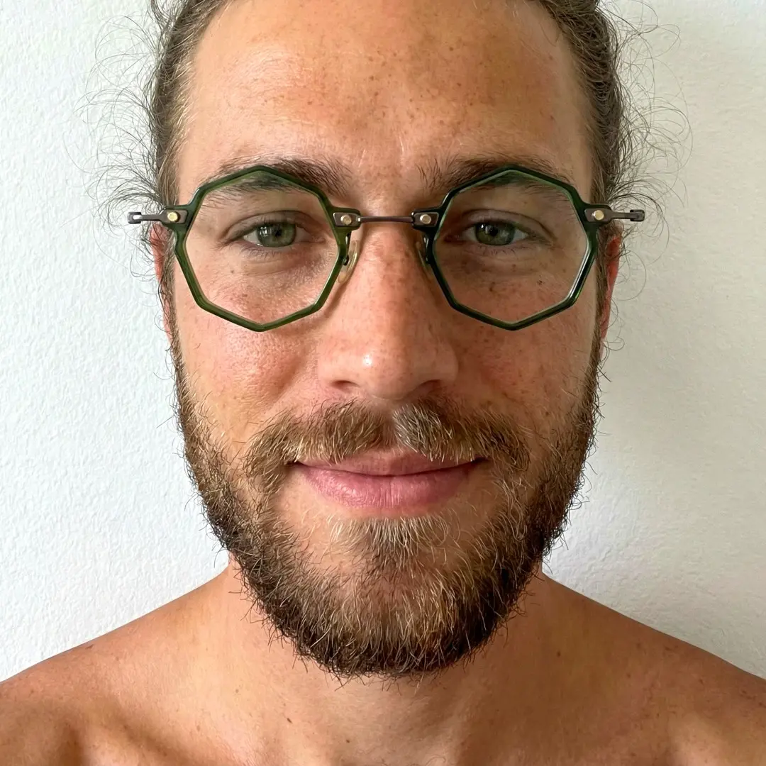 Front view of male wearing green geometric eyeglasses, soft smile, GT0332411