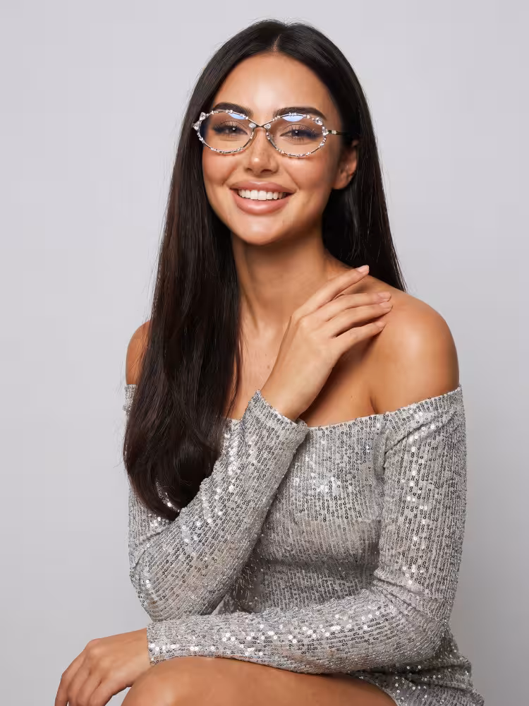 Female model wearing vintage silver oval metal rhinestone eyeglasses with silver off-shoulder sequin dress in plain gray studio. SPU:OM0292512