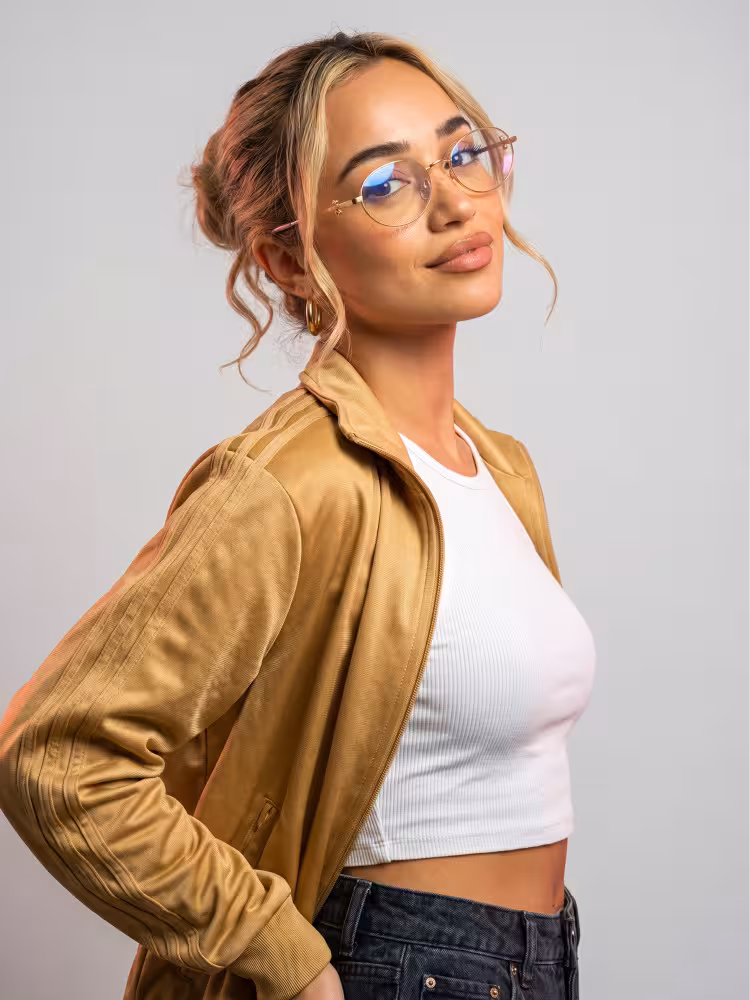 Female model wearing vintage gold oval metal eyeglasses indoors against a plain grey background. SPU: OM0352512