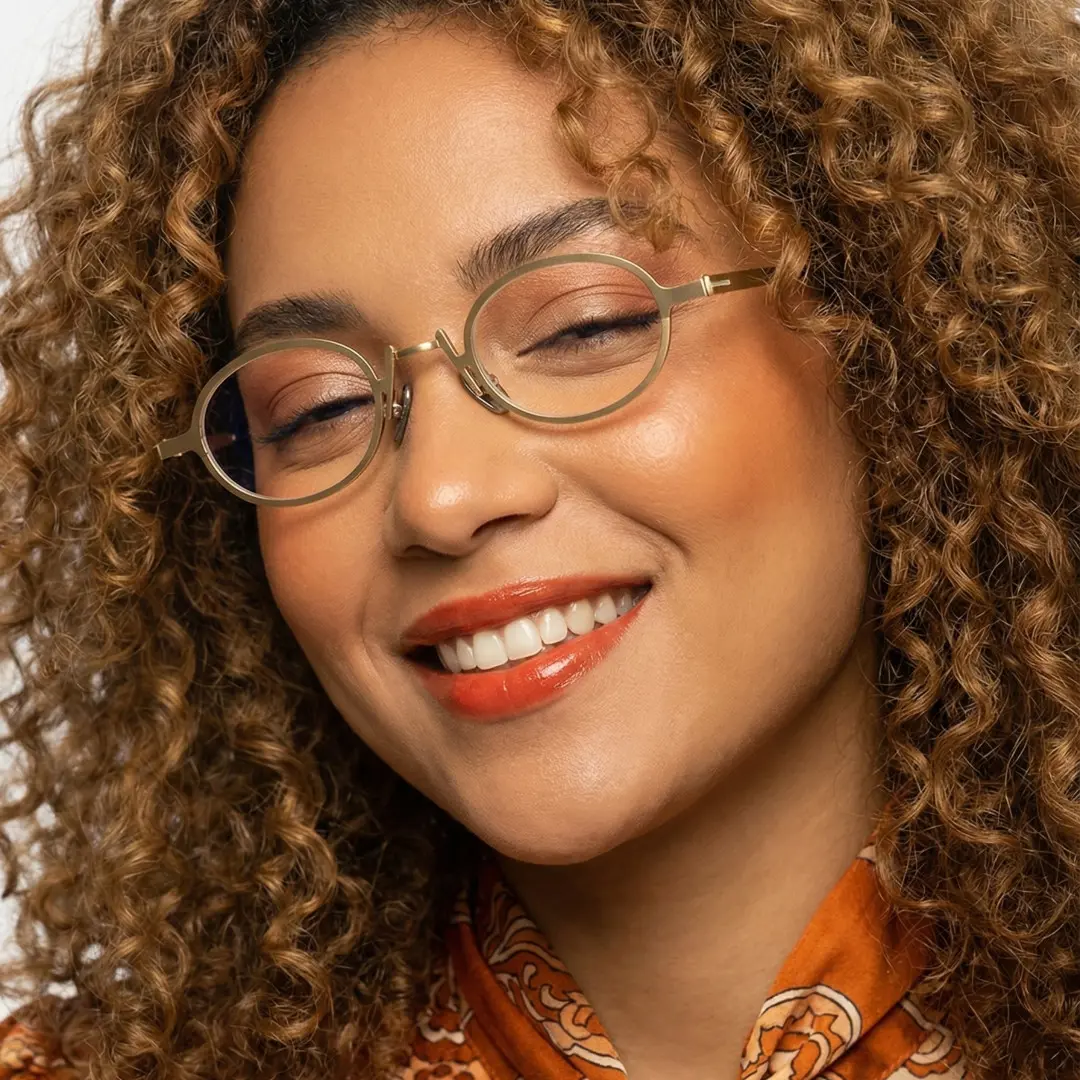 Front view of female wearing vintage gold oval eyeglasses, tilting head, natural smile, OM0592302