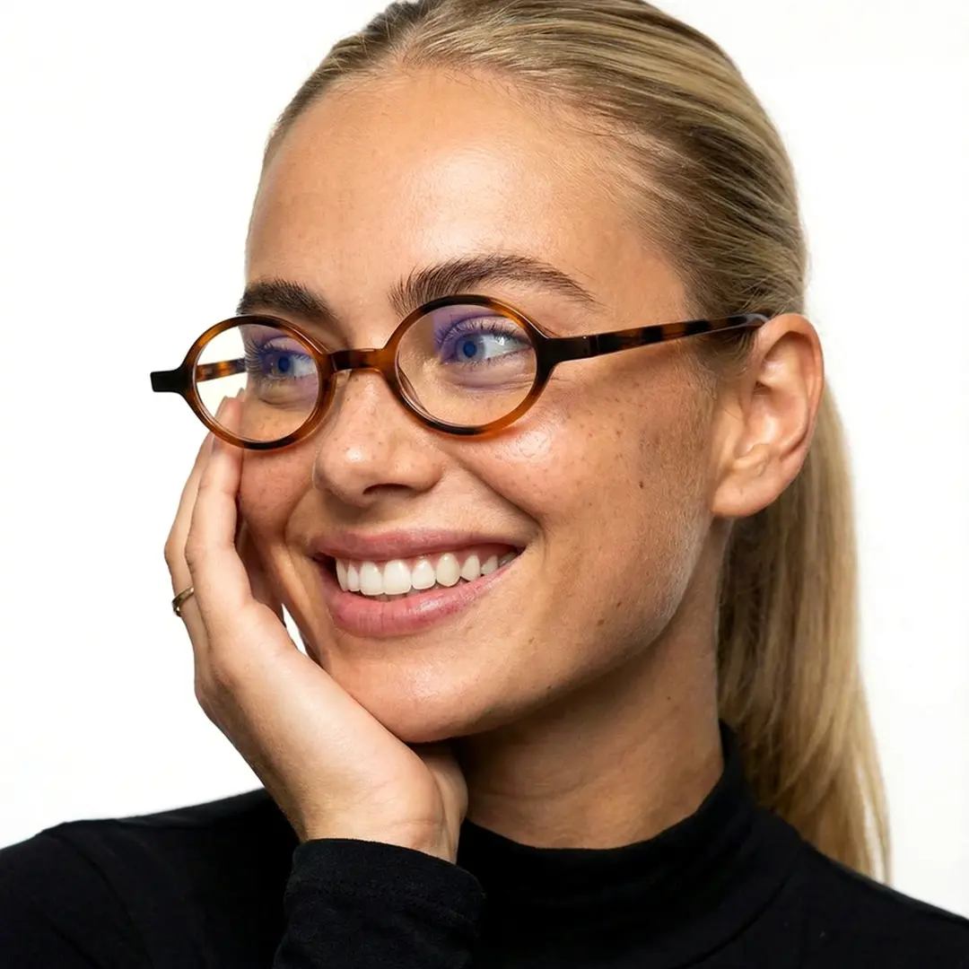 Looking away view of female wearing tortoise oval eyeglasses, resting chin on hand, smiling, OP0142307